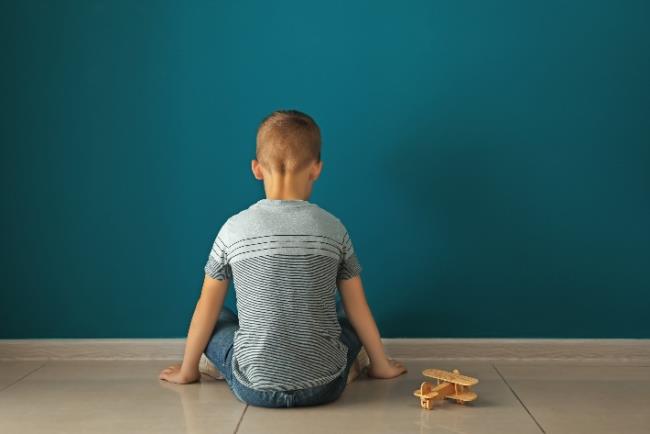 ילד קטן יושב לבד עם גבו לקיר כדימוי לילד שעלול לסבול מאוטיזם ולהימנע מאינטראקציה חברתית